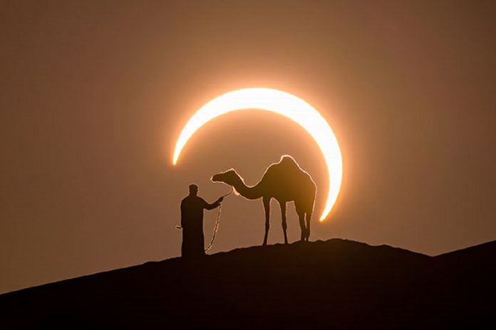 O click perfeito: homem e dromedário no meio do deserto emoldurados por um eclipse solar