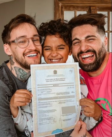 revistapazes.com - Pais comemoram fim de processo de adoção mostrando nova certidão de nascimento para filho